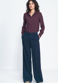 Bordowa koszula w białe kropki, z długimi rękawami i kołnierzykiem, zestawiona z granatowymi spodniami o wysokim stanie i szerokich nogawkach.