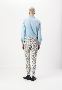 Lyseblå denimskjorte med knappmansjetter, kombinert med hvite bukser med svarte svinnende paisley-mønstre, og svarte ankelstøvler.