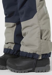 Donkerblauwe en lichtgrijze geïsoleerde sneeuwbroek met elastische boorden, in combinatie met zwarte waterdichte laarzen met een gestructureerde zool.