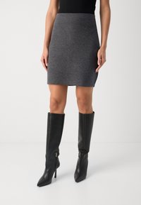 Grijze gebreide rok met een aansluitend ontwerp, gecombineerd met hoge zwarte leren laarzen met een puntige neus en ritsdetails.