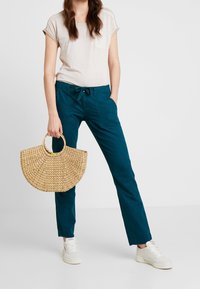 Tealbyxor med en avslappnad passform och framfickor, i kombination med en ljusbeige kortärmad topp. Håller en rund vävd stråväska.