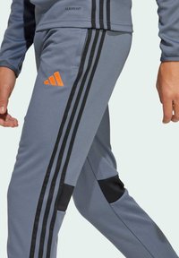 Graue Trainingshose mit schwarzen Streifen, orangefarbenem Logo und strukturierten Akzenten. Sie hat eine schmale Passform und ein zulaufendes Bein Design.