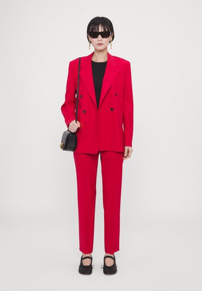 Blazer rouge à double boutonnage avec pantalon assorti ; coupe ajustée, tissu lisse. Un top noir, un petit sac à main et des lunettes de soleil rondes/accessoirisent le look.
