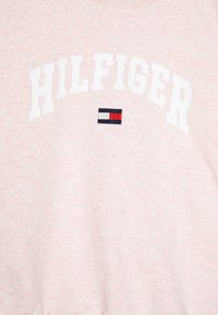 Sweatshirt rose clair en tissu texturé. Présente "HILFIGER" en lettres blanches en gras et un petit logo brodé en bleu, rouge et blanc.