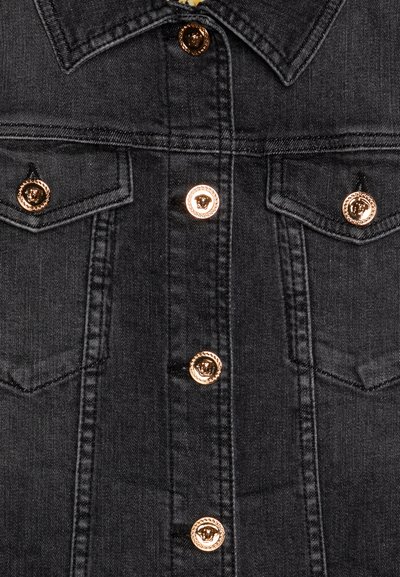 Chaqueta de mezclilla negra con botones dorados, dobles bolsillos en el pecho y un diseño de cuello clásico. Tejido texturizado con costuras visibles.
