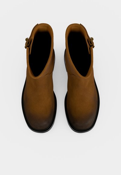 Paire de bottines en cuir marron avec semelles noires, vues de dessus sur un fond blanc.