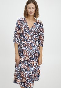 Blumenkleid mit 3/4-Ärmeln, das eine Mischung aus Marineblau, Rost und Cremefarben zeigt. Weicher Stoff mit fließender Silhouette.
