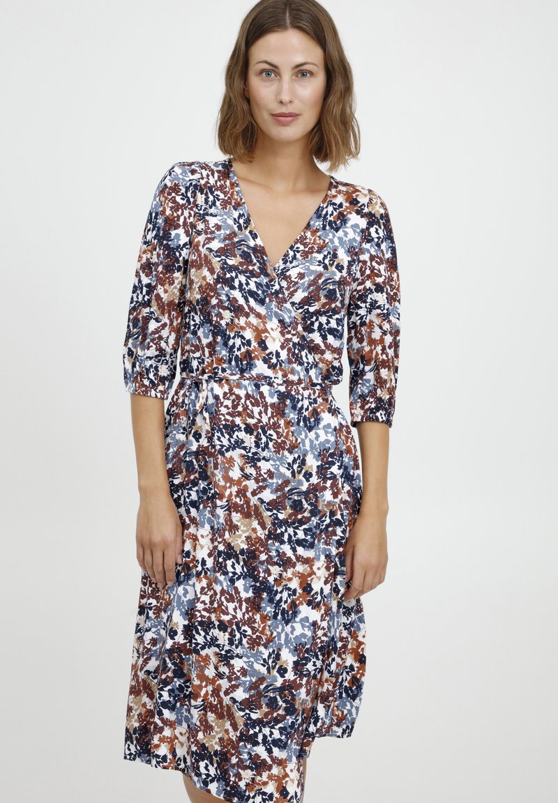 Blumenkleid mit 3/4-Ärmeln, das eine Mischung aus Marineblau, Rost und Cremefarben zeigt. Weicher Stoff mit fließender Silhouette.