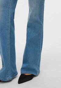 Vaqueros acampanados azul claro con una textura suave de mezclilla y un acabado limpio. Combinados con elegantes tacones negros de punta fina.