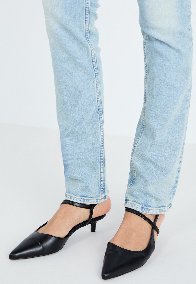 Décolleté nere in pelle con punta affilata e tacco kitten basso, con cinturino alla caviglia, abbinate a jeans azzurri chiari.