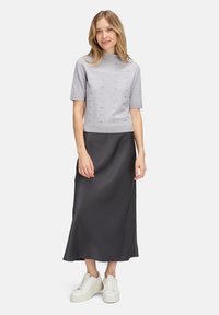 Szara krótka bluzka dzianinowa z detalami w formie oczek, zestawiona z długą czarną satynową spódnicą i białymi sneakersami. Prosta, nowoczesna sylwetka.