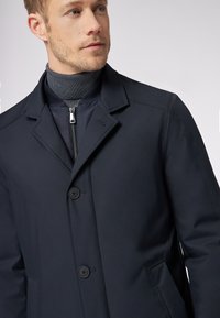 Cappotto navy con tessuto testurizzato, design monopetto e due bottoni. Presenta un interno con zip e tasche laterali.