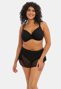 Ensemble de lingerie noire comprenant un soutien-gorge armaturé à motifs et une jupe transparente assortie. Le tissu est texturé avec des motifs géométriques et des bords délicats.