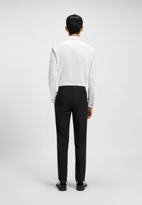 Weißes Langarmhemd mit glatter Textur, kombiniert mit schwarzen Hosen in taillierter Passform und dezenten Gesäßtaschen. Schwarze Schuhe runden den Look ab.
