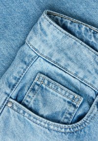 Nahaufnahme von hellblauen Jeans aus Denim, die eine Vordertasche mit einer kleineren Münztasche innen zeigen.