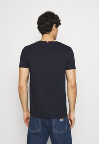 Námořnická modrá tričko s krátkým rukávem vyrobené z bavlny, s klasickým kulatým výstřihem a malou tříbarevnou visačkou na zadní straně. Jednoduchý a přiléhavý design.