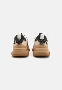 Chunky athletic sneakers with a beige mesh upper, black accents, and a textured tan rubber sole. Features pull tabs for easy wear.