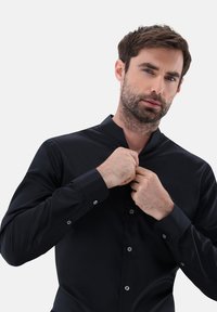 Schwarzes Langarmshirt mit Stehkragen, aus glattem Stoff gefertigt, mit Knopfverschlüssen und taillierter Passform.