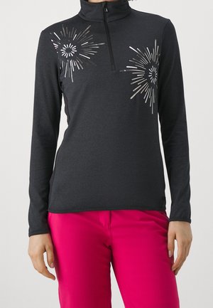 Vrouw draagt een donkergrijs langärmelig vest met zilveren stervormige prints en felroze broek.