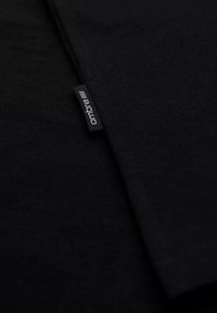 Černé bavlněné tričko s hladkou texturou; na boku má malou cedulku s nápisem "ombre". Jednoduchý, minimalistický design.