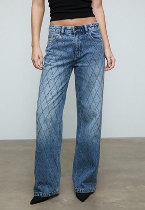 Helle blaue Jeans aus Denim mit Rautenmustern und Verzierungen, weit geschnitten, im klassischen Fünf-Taschen-Design, kombiniert mit spitzen schwarzen Schuhen.