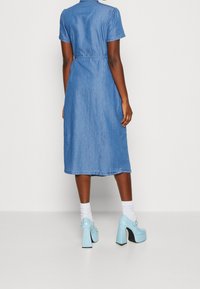 Denimmidiklänning med korta ärmar, bälte i midjan och raka former. Stylad med ljusblå plattformsspetsar och vita strumpor.