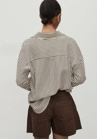 Chemise à manches longues rayée en beige et marron foncé, présentant un ourlet arrondi et une coupe décontractée, associée à un short marron. Vue de dos.