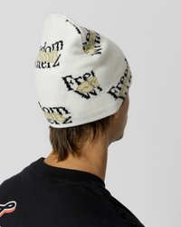 Gorro de punto blanco con texto "Libertad" en negro y dorado, y patrones gráficos. Textura suave, diseño ajustado y forma ligeramente cónica.
