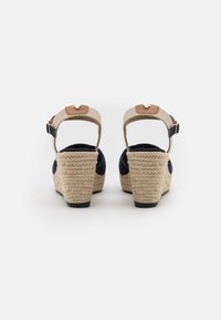 Sandales compensées bleu marine avec des brides tissées texturées beige et un accent marron clair. Elles disposent d'une boucle ajustable et d'un talon enveloppé de jute.