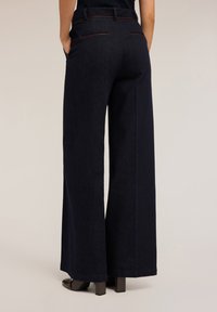 Široké tmavě modré džíny s hladkou texturou, které mají zadní kapsy a jemné kontrastní prošití.