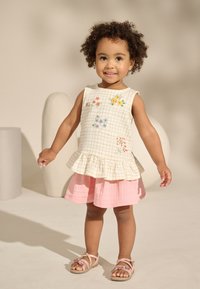 Lapse riietus, mis koosneb beežist ruudulise mustriga särgist, millel on värviline lilleline tikand, ja roosast tekstuurse seelikuga. Komplektis roosad sandaalid.