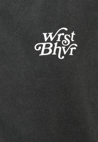 Černý bavlněný oděv se stylizovaným bílým logem "wrst Bhvr" umístěným na levé straně. Měkká textura, žádné další vzory.