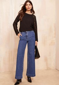 Maglietta nera a maniche lunghe con dettagli in pizzo, abbinata a jeans in denim blu a vita alta e gamba larga. Una borsa nera e stivali con tacco completano il look.