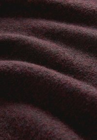 Tessuto texturizzato di un profondo bordeaux con sottili variazioni. Il materiale appare morbido con una superficie leggermente pelosa e dolci increspature.