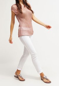 Texturovaný top v růžovozlaté barvě, bílé úzké kalhoty a hnědé žabky se stříbrnými detaily. Top má krátké rukávy a vlnitý vzor.