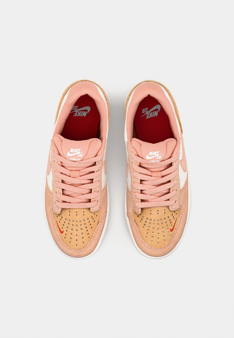 Zapatillas Nike en tonos rosa claro y ante beige; presentan detalles en blanco, cordones rosas, caja del dedo perforada y detalles del logotipo en rojo.