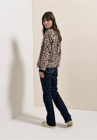 Rosa Pullover mit Leopardenmuster und langen Ärmeln, kombiniert mit dunkelblauer Jeans und hellen Schuhen, aus leichtem Winkel betrachtet.