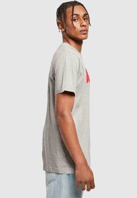 Graues Baumwoll-T-Shirt mit kurzen Ärmeln, das einen roten Logo-Schriftzug auf der Vorderseite zeigt. Reguläre Passform mit Rundhalsausschnitt und weichem Textil.