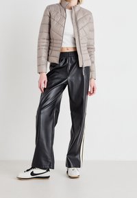 Light beige quilted jacket with stand collar and zip closure, paired with black faux-leather pants featuring side stripes and white sneakers.