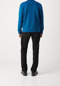 Felpa blu con scollo rotondo e polsini a coste, abbinata a jeans neri con cinque tasche e gamba dritta.