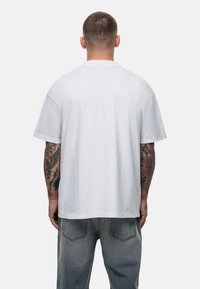 Witte katoenen t-shirt met een relaxte pasvorm, korte mouwen en een rechte zoom. Achteraan is een simpele, gladde textuur zichtbaar.