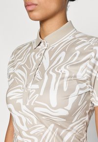 Beige polo tričko s bílým abstraktním vzorem, s klasickým límcem, knoflíky a krátkými rukávy, vyrobené z hladkého, lehkého materiálu.