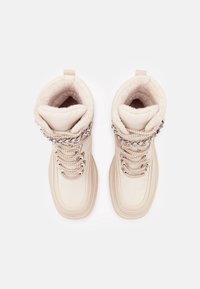 Bottes d'hiver beiges avec dessus texturé, doublure en fausse fourrure et détail de lacets avec chaîne argentée. Bout rond et semelle à couches.