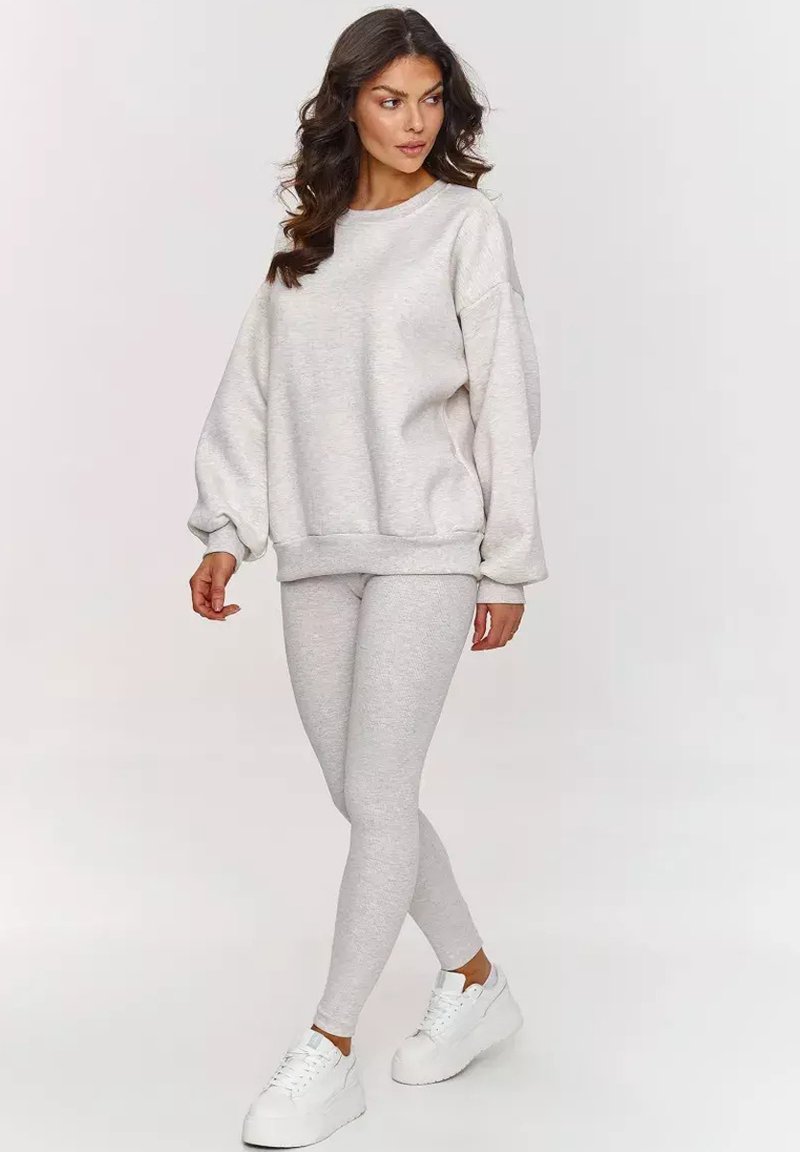 Jasnoszara bluza z opadającymi ramionami, ribbowym dołem i dopasowanymi legginsami. Materiał wydaje się miękki i teksturowany. Noszona z białymi trampkami.