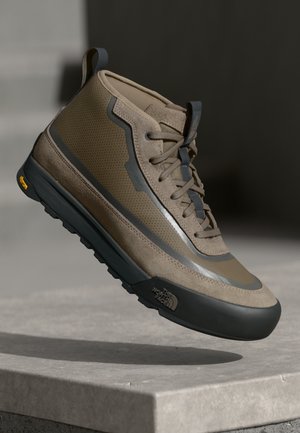 Brun høyhælte tursko med teksturert semsket skinn og mesh-overdel, grå detaljer og en svart Vibram-såle med gule innslag.