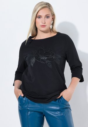T-shirt noir à manches longues avec un motif floral embellie de sequins. Associé à un pantalon bleu brillant, présentant une texture lisse et un bon ajustement.