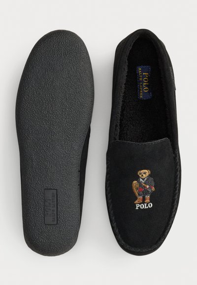 Čierne zamatové papuče s textúrovanou gumovou podrážkou, s výšivkou medvedíka a štítkom "Polo Ralph Lauren" vo vnútri.