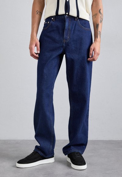 Bredde ben denim bukser i mørkeblå, med kontraststing, forlommer og en afslappet pasform. Kombineret med sorte sneakers.