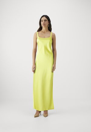 Vestido de satén, sin mangas, de largo hasta el suelo en un brillante color amarillo con escote cuadrado. Combinado con zapatos de tacón alto beige para crear contraste.