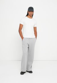 Hvid kortærmet t-shirt, lysegrå sweatpants, sorte sko og en mørkegrå cap. Tøjet er afslappet og komfortabelt i pasformen.